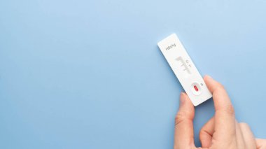 El ele tutuşan Hepatit B Virüs Yüzey Antijen Test kiti mavi arka planda pozitif sonuç verdi. Hepatit B için yapılan taramalarda parmak deliğinden alınan kan örneği kullanılır. Dünya Hepatit Günü.