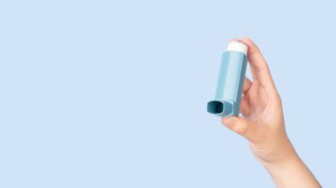 Astım krizi için astım spreyini tutan eller izole edilmiş mavi arka plan. İlaç ürünleri hırıltıyı ve nefes darlığını önlemek ve tedavi etmek için kullanılır. Astıma ya da COPD 'ye neden olur..