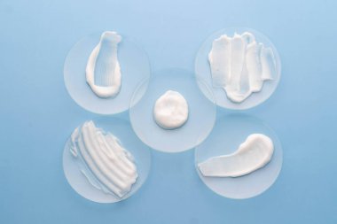 Mavi arka plandaki saat camında beyaz krem lekesi. Laboratuvarda cilt bakımı ürünü örneği var. Güzellik ve kozmetik konsepti.