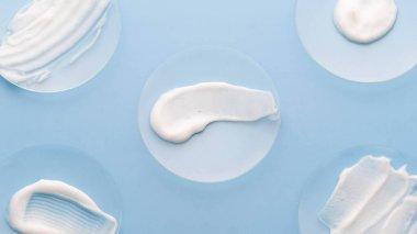 Mavi arka plandaki saat camında nemlendirici beyaz krem lekesi. Laboratuvarda cilt bakımı ürünü örneği var. Güzellik ve kozmetik konsepti.