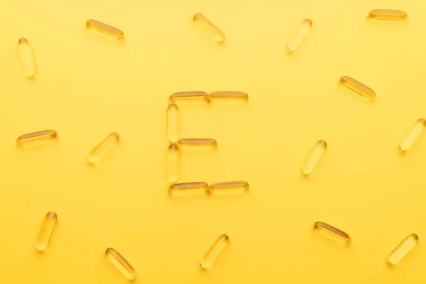 Vitamin E capsules with alphabet letter E on yellow background. Oil Softgel capsule uses for nutritional supplement, hair serum, skincare product and cosmetic ingredient.