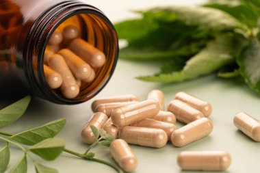 Alternatif ilaç bitkisel kapsüller kahverengi cam şişeden döküldü ve yeşil arka planda taze organik bitki yaprağı var. Doğal bitkiler ve homeopatik destek ürünleri. Kapat..