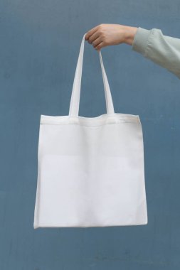 Boş beyaz çanta bez kumaş ve kabzası da tasarım. Mavi metal duvarda kadın el ele tutuşması ya da tekrar kullanılabilir alışveriş torbası. Plastik poşet ve ekoloji konsepti yok. Dikey.