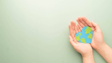 Dünya kalp günü. Yeşil arka planda kağıt üzerine yapılmış toprak haritasıyla kalp şeklini tutan düz bir el yatağı. Kardiyolojinin tıbbi bakım şablonu, Dünya 'nın kutlamaları, aşk ve dünyayı kurtarma..