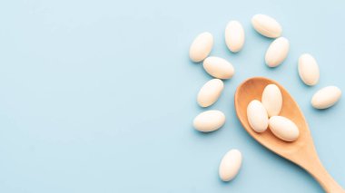 Açık mavi arka planda tahta kaşıkla beyaz yumuşak jelatin kapsüller. Probiyotik takviye, vitamin ve ağrı kesici bağımlılığı için bir şablon. Boşluğu kopyala.