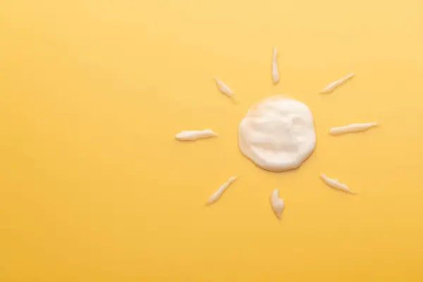 Sunscreen cream texture in sun shape on yellow background. SPF sunblock cream for protect against wrinkles, discoloration and skin cancer. Daily skincare products for sun protection.
