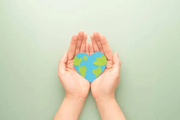 World heart day. Flat lay of hands holding heart shape with earth map made by paper on green background. Template for cardiology medical care, earth\'s day celebration, love and save the earth.