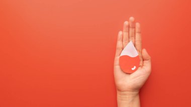 Kırmızı zemin üzerinde kan olan kan damlası şeklini tutan insan eli. Anemi, orak hücre hastalığı, hemofili, lösemi ve ITP gibi hematolojik bozuklukların farkındalığı. Kan bağışı..