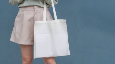 Boş beyaz çanta bez kumaş ve kabzası da tasarım. Mavi metal duvara karşı eko ya da tekrar kullanılabilir alışveriş torbası tutan kadına yakın durun. Plastik poşet ve ekoloji konsepti yok.