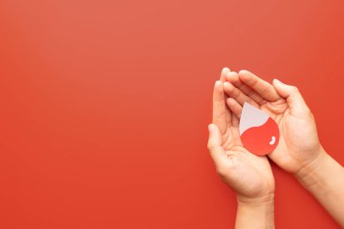 Kırmızı zemin üzerinde kan olan kan damlası şeklini tutan insan eli. Anemi, orak hücre hastalığı, hemofili, lösemi ve ITP gibi hematolojik bozuklukların farkındalığı. Kan bağışı..