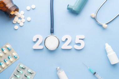 2025 Sağlık ve Sağlık Hizmetleri ve Sağlık Konsepti Yeni Yıl Sancağınız kutlu olsun. Doktor hapları, şırınga, aşı şişesi, göz damlası, antibiyotikler ve masa mavi arka planda 2025 numaralı beyaz madde ile stetoskop..