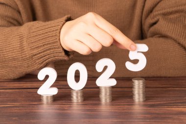 2025 yılbaşı tasarruf ve finansal planlama konsepti. Kadın eli 2025 numarayı bozuk para yığınına koyuyor. İş büyümesi, vergi ödemesi, yatırım ve bankacılık için yaratıcı bir fikir.