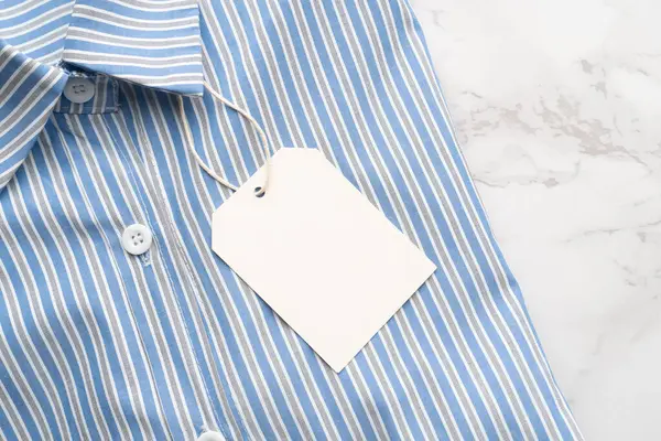 Mermer zemin üzerinde boş etiket etiketi olan mavi çizgili gömlek. Tasarım için hazırlan.