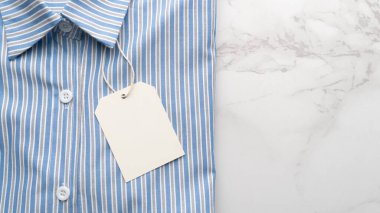 Mermer zemin üzerinde boş etiket etiketi olan mavi çizgili gömlek. Tasarım için hazırlan.