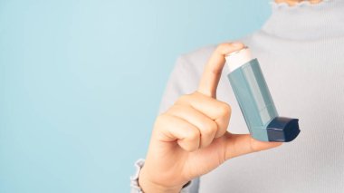 Astım spreyi kullanan bir kadın açık mavi arka planda astım krizi geçiriyor. İlaç ürünleri hırıltıyı önlemek ve tedavi etmek için kullanılır ve nefes darlığı astıma ya da COPD 'ye neden olur. Kapat..