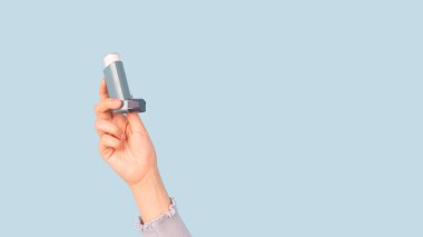 Astım spreyi tutan kadın açık mavi arka planda. İlaç ürünleri hırıltıyı ve nefes darlığını önlemek ve tedavi etmek için kullanılır. Astıma ya da COPD 'ye neden olur..