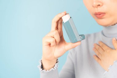 Young female using blue asthma inhaler for relief asthma attack. Pharmaceutical products is used to prevent and treat wheezing and shortness of breath caused asthma or COPD. Close up.