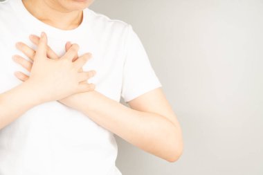 Gri arka planda göğüs ağrısı çeken genç bir kadın. Göğüs ağrısı anjini, kalp krizi, GERD ya da kostokondritin nedenleri. Sağlık ve kardiyolojik konsept. Kapat..