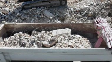 Bir buldozer kovası inşaat alanından taşınmak üzere bir kamyon konteynırına taş ve inşaat atığı doldurur..