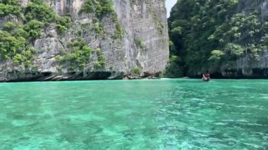 Bir tekne, yüksek dağlar ve yemyeşil ağaçlarla çevrili bir gölün sakin sularında huzur içinde süzülür ve çarpıcı bir doğal manzara yaratır..