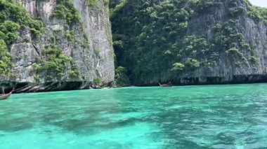 Bir tekne, yüksek dağlar ve yemyeşil ağaçlarla çevrili bir gölün sakin sularında huzur içinde süzülür ve çarpıcı bir doğal manzara yaratır..