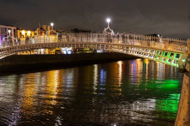 Dublin şehir merkezindeki Liffey Nehri üzerindeki ünlü yaya Penny Hapenny Köprüsü gece görüşü.