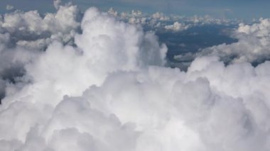 Havadan bakıldığında mavi gökyüzüne karşı beyaz kabarık bulutlar ve aşağıdaki yemyeşil araziler görülüyor..