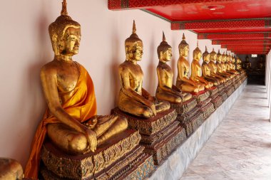 Huzurlu bir tapınak ortamında huzur ve maneviyatı simgeleyen bir sıra altın Buda heykeli..