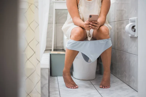 Çamaşırlarıyla Banyoda Oturan Bir Kadın Akıllı Telefonunu Kullanıyor — Stok fotoğraf