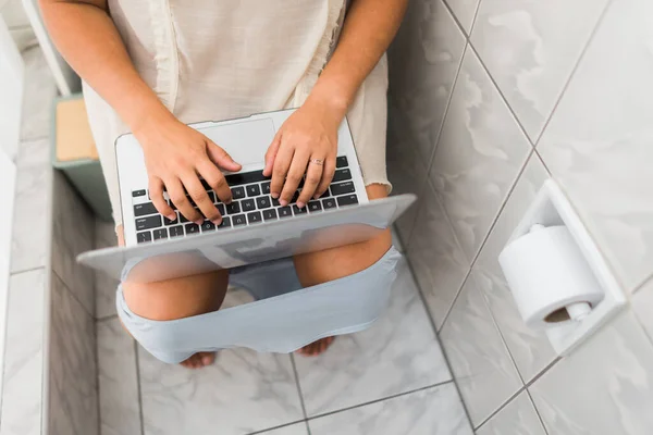 一个女人在浴室里用她的个人电脑坐在马桶上的头像 — 图库照片