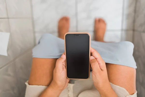 a Caucasian woman communicating remotely with her smart phone sitting in the bathroom of her home in her sleepwear, underwear down, relaxed.
