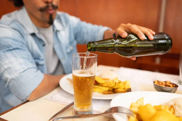 Tanımlanamayan bir adam yeşil bir şişeden altın bir birayı masaya Peru yemeği tabaklarıyla oturmuş bir bardağa dolduruyor..