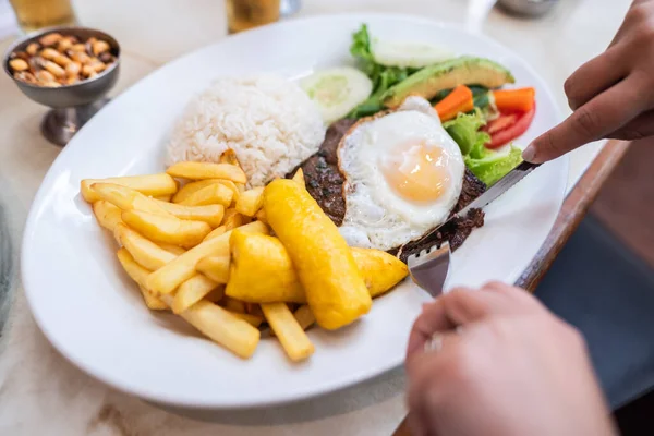 Bilinmeyen birinin fakirlere bistek kestiği gerçek bir görüntü, geleneksel bir Peru tabağı kızarmış yeşil muz, patates kızartması ve monte edilmiş yumurta. Yanında pilav ve akşamdan kalma salatası var..