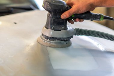 Araba tamirhanesinde araba cilalayan bir adamın elinde öğütücü..