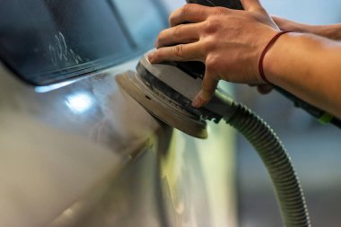 Araba tamirhanesinde araba cilalayan bir adamın elinde öğütücü..