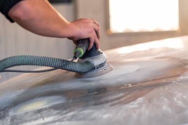 Araba tamirhanesinde araba cilalayan bir adamın elinde öğütücü..