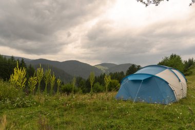 Çimen tarlasında kamp manzarası. Ormanın arka planı, dağlar ve doğal parktaki günbatımı gökyüzü..