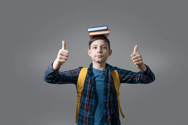 funny kid or pupil in casual clothes with school bag and books showing thumb-up gesture, study and education concept