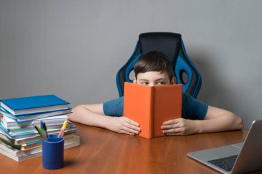 Masasında oturup ödev, eğitim ve eğitim konseptini hazırlayan açık ders kitabı olan çocuk öğrenci ya da çocuk.