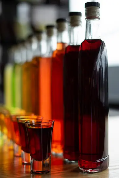 Şişelere ve meyve alkollü tentürle bardaklara yakın çekim ya da masada ev yapımı üzüm şarabı. Lokantada tatlı dut alkolü