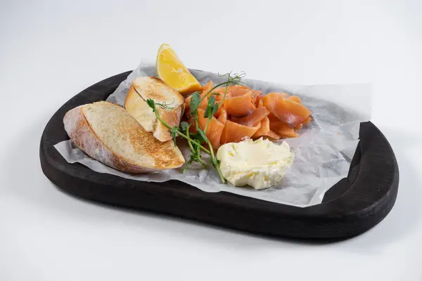 Lezzetli restoran atıştırmalıkları, somon, kızarmış ekmek ve krem peyniri ahşap tabakta süslemeli otlar ve limon. Beyaz arka planda taze balık ve kızarmış bruschetta. Sağlıklı beslenme
