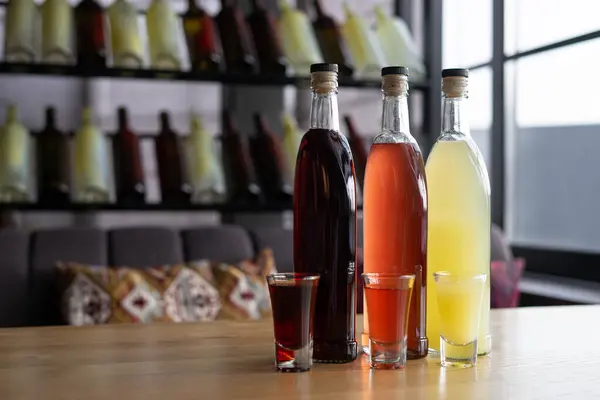 Bardaki masada bulunan doğal malzemelerden alınmış tatlı meyve alkollü tentürle dolu şişeler. Ev yapımı dut alkolü ya da şarap. Restoranda içeceklerle dolu bardaklar.