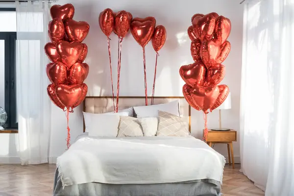 Yastıklı yatak ve battaniyeli oda içi açık kırmızı balonlarla süslenmiş kalp şeklinde, Sevgililer Günü kutlaması konsepti