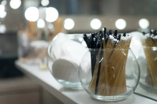 Güzellik salonundaki rafta duran cam vazodaki kaş fırçaları ve aplikatörlere özen gösterin. Makyaj veya kirpik uzatma için kozmetik araçlar