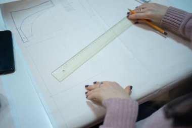 Atölyedeki masada otururken terzinin çalışmasını ve kağıt üzerinde dikiş desenlerini kesmiş. Kalem ve cetvel çizimli terzi elleri.