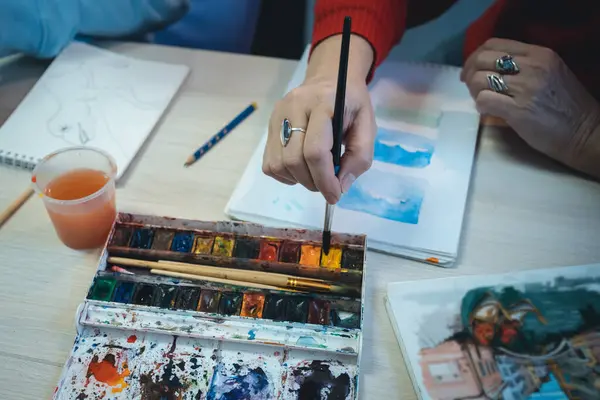 Boyacı el fırçası ile boya ve atölyedeki çalışma masasındaki çizim defterinde öğrenciye nasıl çizim yapılacağını gösteriyor. Sanat okulunda öğretmeniyle resim dersinde oturan çocuk manzarası.