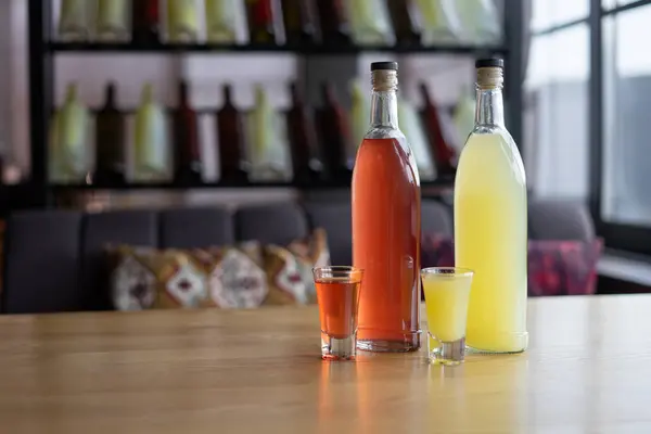 Bardaki ahşap masada bulunan doğal malzemelerden elde edilen alkollü meyve tentürü şişeleri. Ev yapımı dut alkolü. Restoranda içeceklerle dolu bardaklar.