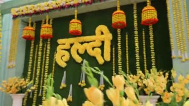 Indian wedding decoration with Haldi (Meaning - turmeric) . written text using yellow marigold flowers on green leaves placed on beautiful vibrant curtain.