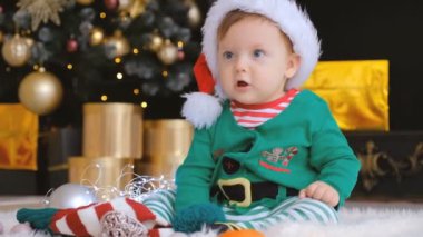 Noel Baba şapkalı bir çocuk Noel ağacının yanında oturuyor ve içinde hediye olan bir kutuyu açıyor. Aile çemberinde Noel 'i bekliyorum..