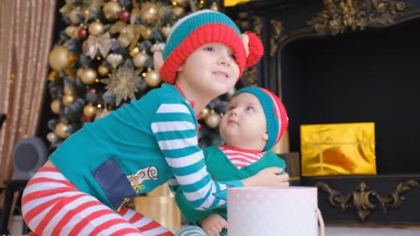 Aan Vooravond Van Vakantie Zitten Twee Kinderen Kerstmutsen Bij Kerstboom — Stockvideo